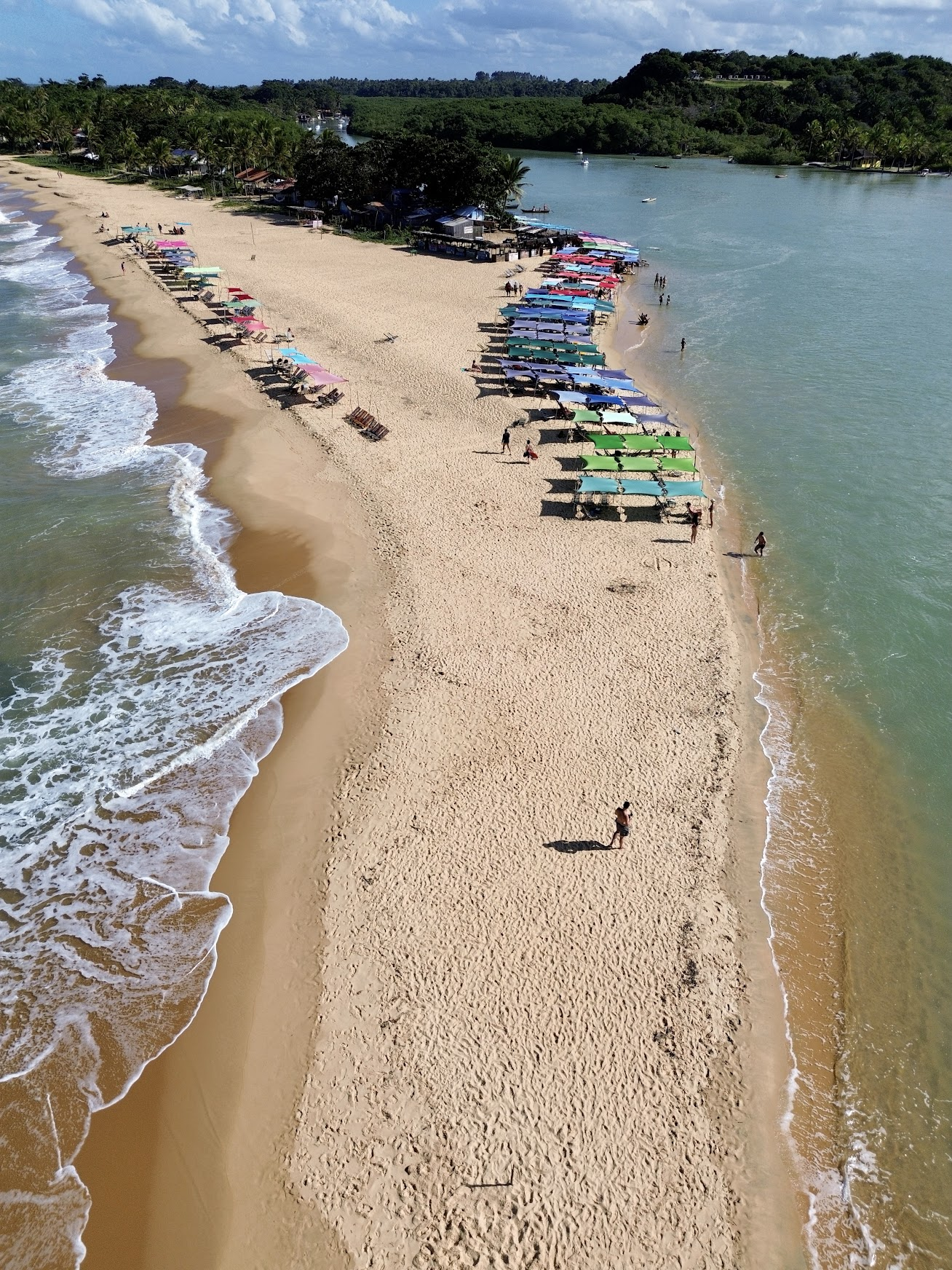 Turistas aproveitando o banho de rio no encontro com o mar na Praia da Barra em Caraíva, com cadeiras na água